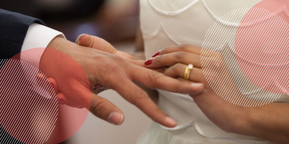 Mão feminina colocando aliança de casamento em mão masculina