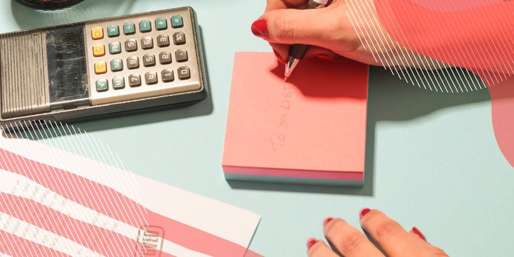 Pessoa anotando lista de tarefas em post it cor de rosa sobre mesa de escritório