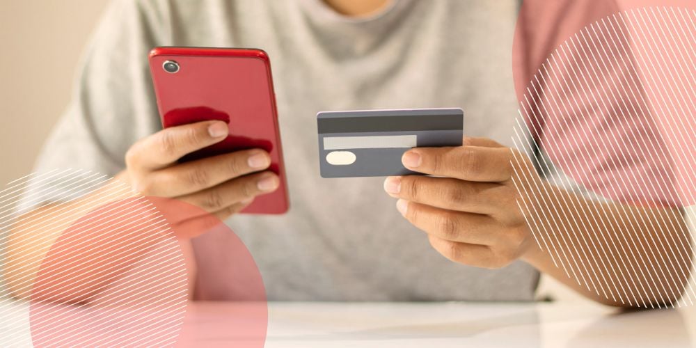 Homem segurando celular vermelho e cartão de vale-refeição nas mãos