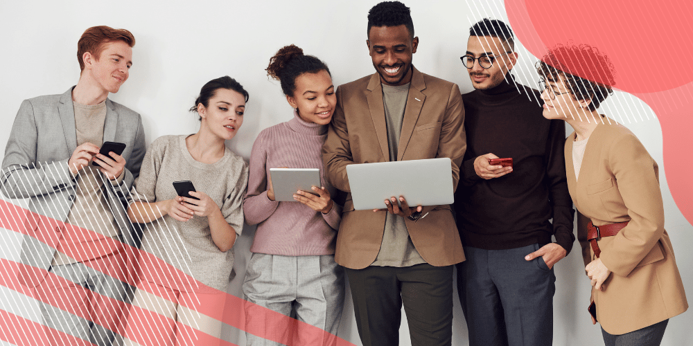 Grupo diverso de seis colaboradores olhando o laptop nas mãos do colega mais alto, no centro da imagem.